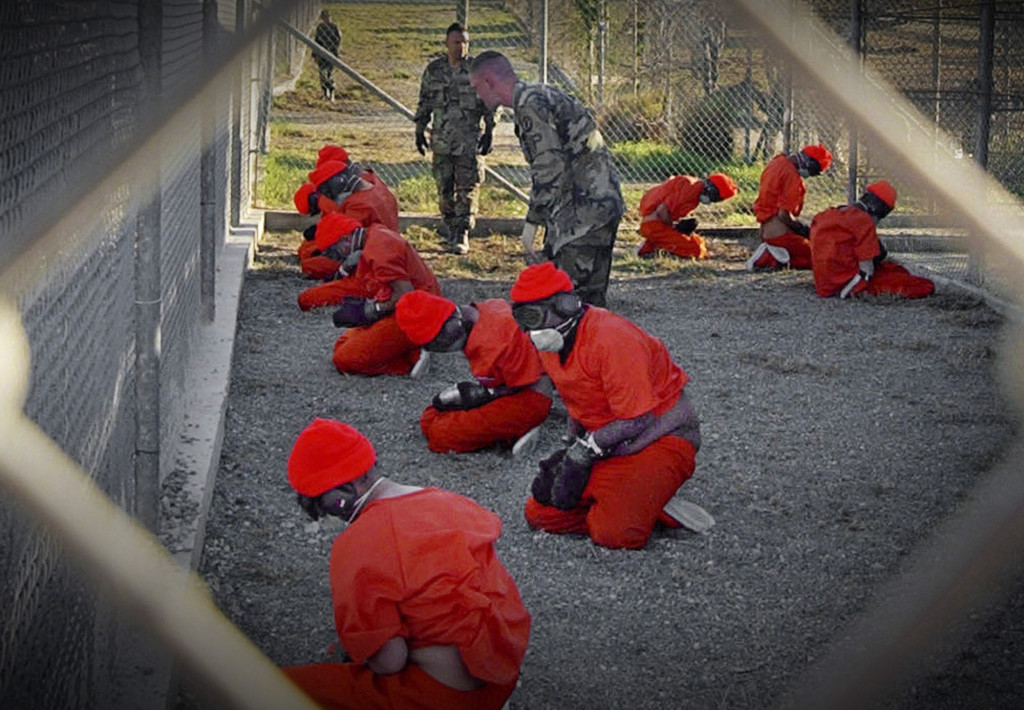 ap foto : ap : ** file ** in this jan. 11, 2002 file photo, released by the department of defense, detainees wearing orange jump suits sit in a holding area as military police patrol during in-processing at the temporary detention facility camp x-ray on guantanamo bay u.s. naval base in cuba.  (ap photo/u.s. navy, shane t.mccoy, file) a jan. 11, 2002 file photo - released by the department of defense ap provides access to this publicly distributed handout photo to be used only to illustrate news reporting or commentary on the facts or events depicted in this image guantanamo politic automatarkiverad